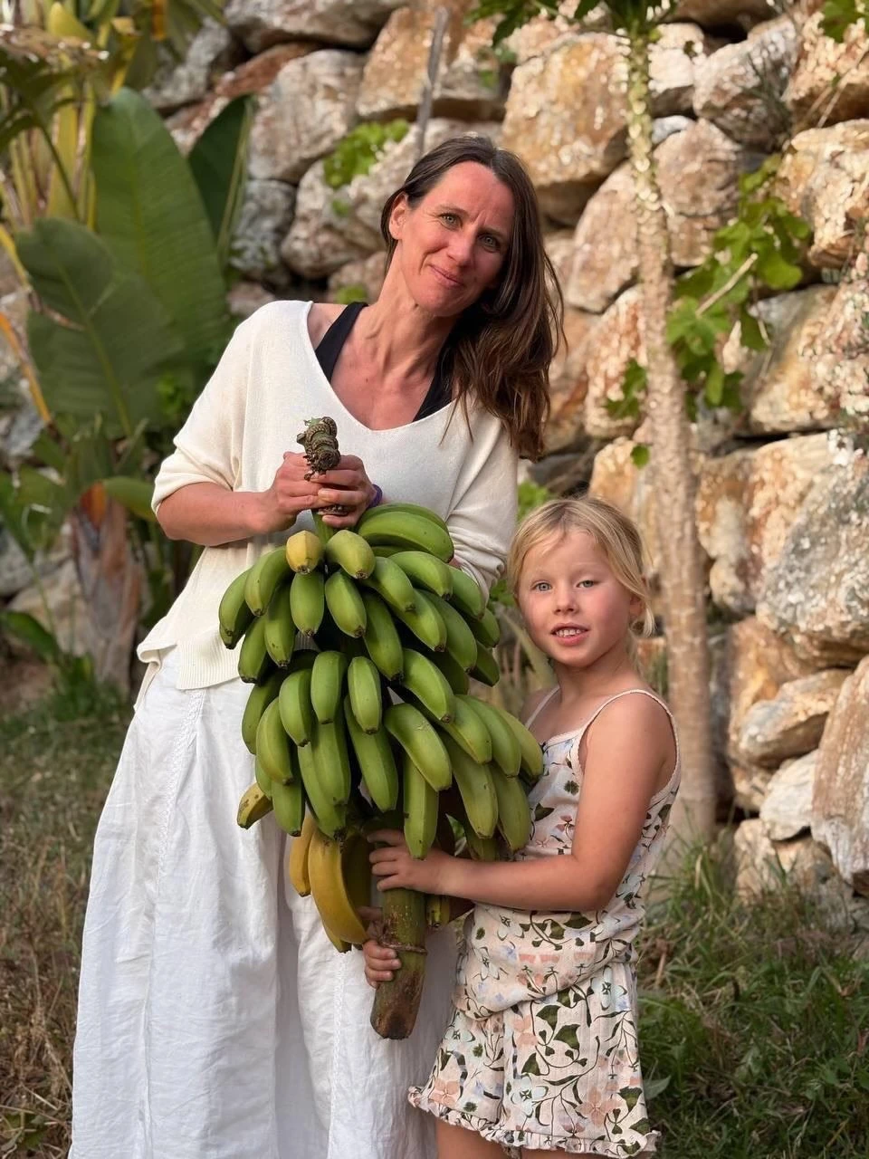 Eine Frau und ein Kind mit einer großen Bananenstaude im Garten